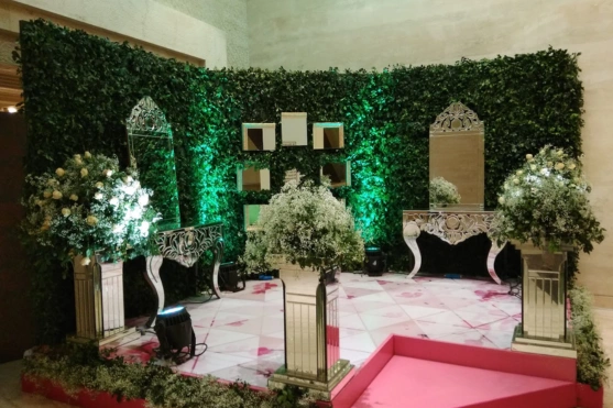 Elegant event setup with ivy wall, white floral arrangements, and stylish benches on a patterned floor.