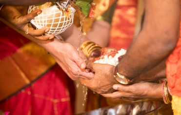 A man and woman join hands, contributing to a bowl, symbolizing a shared moment in their wedding.